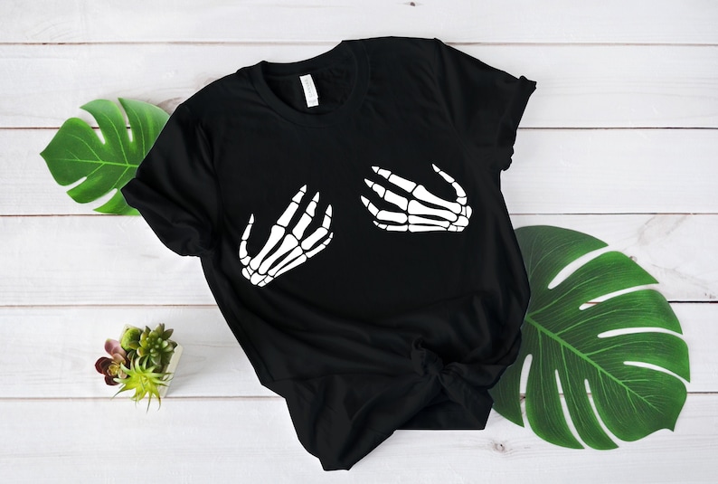 Puede incluir: Camiseta negra con un gr&aacute;fico de mano de esqueleto blanco en la parte delantera. Las manos est&aacute;n en posici&oacute;n de abrazo.