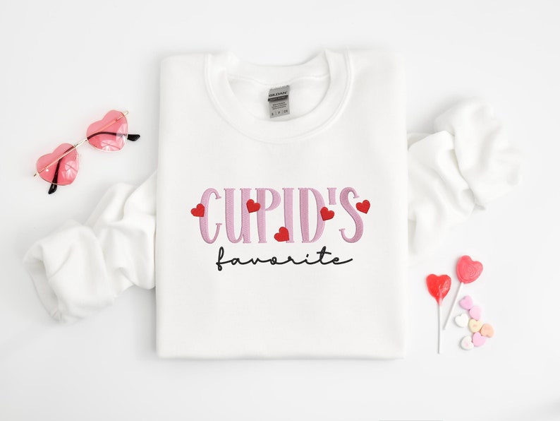May include: White sweatshirt with the text "CUPID'S favorite" in pink lettering with red hearts.