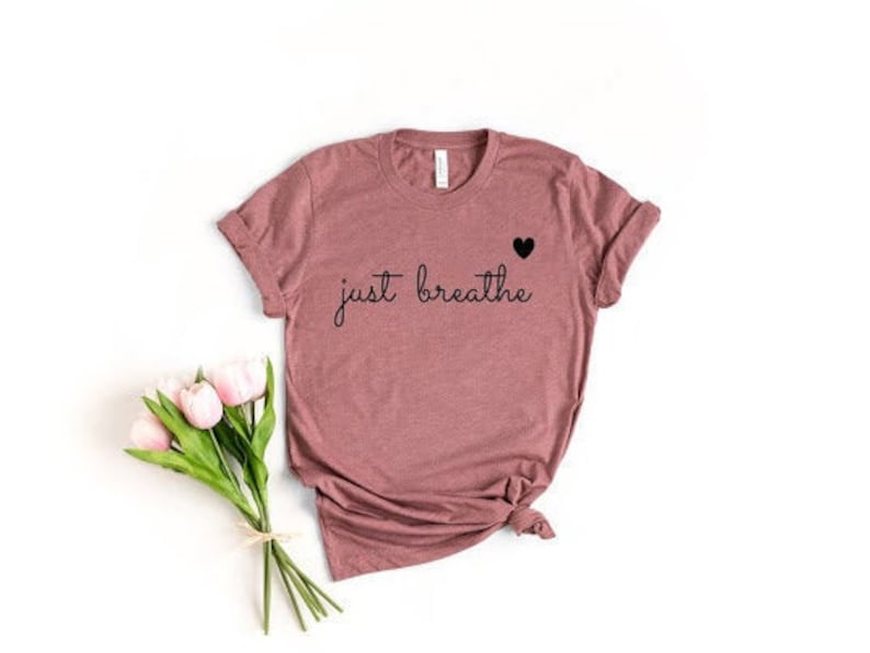 May include: A mauve colored t-shirt with the text "just breathe" and a small black heart above the text.