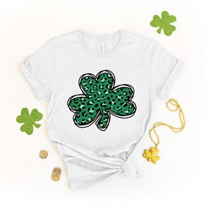 May include: White t-shirt with a green shamrock design. The shamrock is filled with a leopard print pattern.