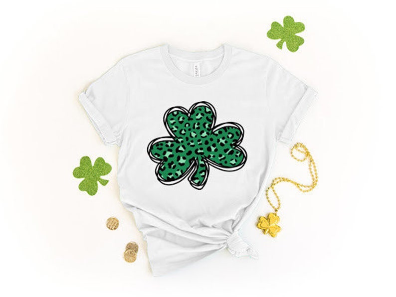 May include: White t-shirt with a green shamrock design. The shamrock is filled with a leopard print pattern.