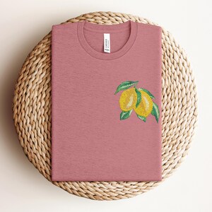 Puede incluir: Una camiseta rosa con un gr&aacute;fico de lim&oacute;n. Los limones son amarillos con hojas verdes.