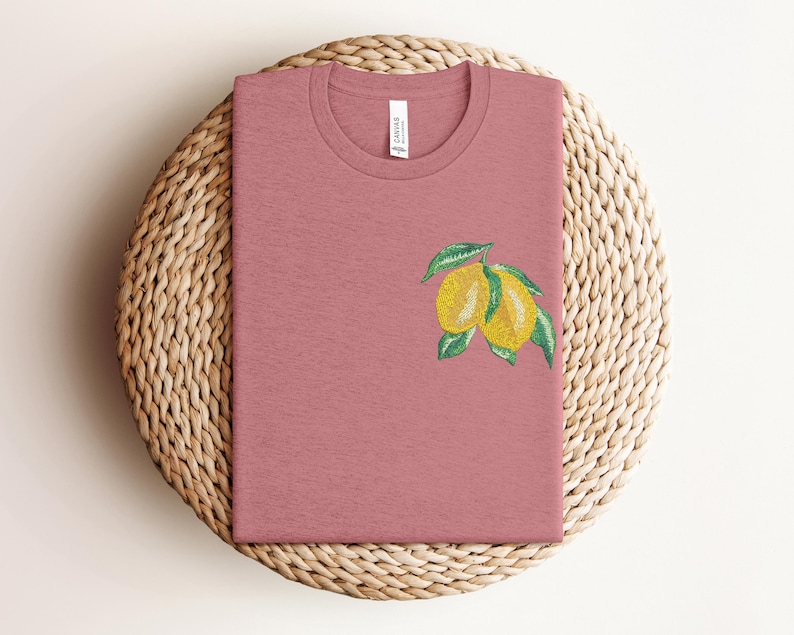 Puede incluir: Una camiseta rosa con un gr&aacute;fico de lim&oacute;n. Los limones son amarillos con hojas verdes.