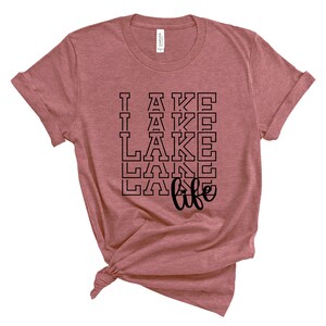 May include: A heather pink t-shirt with a black graphic that says "I  lake life" with the word "lake" repeated four times in a stacked, varsity-style font.