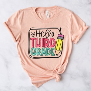 May include: A peach-colored t-shirt with the text "Hello Third Grade" in colorful letters and a pencil graphic.