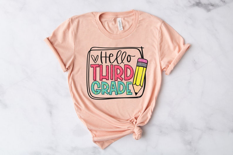 May include: A peach-colored t-shirt with the text "Hello Third Grade" in colorful letters and a pencil graphic.