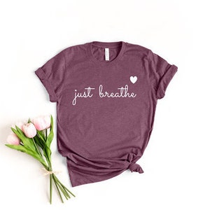 May include: A maroon t-shirt with the text "just breathe" in white script and a small white heart above the text.