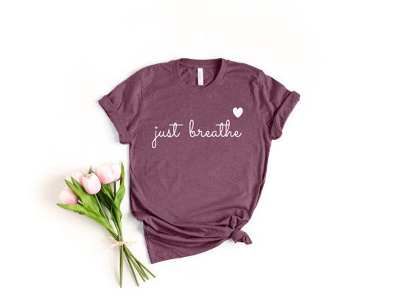 May include: A maroon t-shirt with the text "just breathe" in white script and a small white heart above the text.