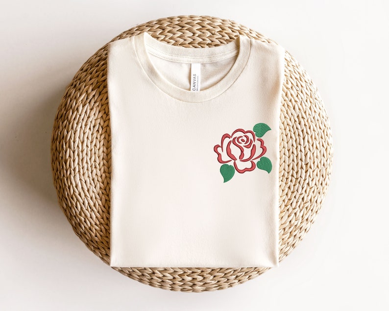 May include: A white t-shirt with a red rose graphic. The rose is stylized and has a green stem and leaves.