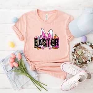 May include: A pink t-shirt with a graphic of bunny ears and the text "Happy Easter" in a colorful, patterned box.