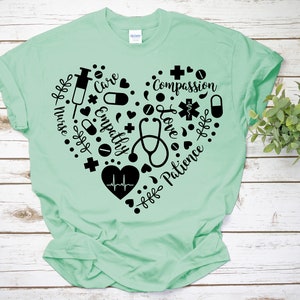 Puede incluir: Una camiseta verde claro con un dise&ntilde;o de coraz&oacute;n negro. El coraz&oacute;n est&aacute; lleno de s&iacute;mbolos m&eacute;dicos y las palabras "Enfermera", "Cuidado", "Empat&iacute;a", "Amor", "Compasi&oacute;n", "Paciencia".