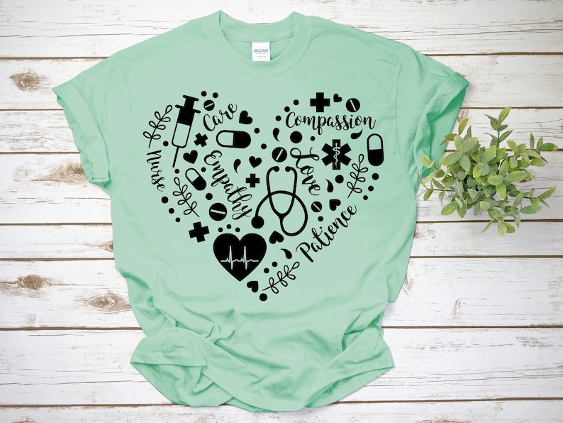 Puede incluir: Una camiseta verde claro con un dise&ntilde;o de coraz&oacute;n negro. El coraz&oacute;n est&aacute; lleno de s&iacute;mbolos m&eacute;dicos y las palabras "Enfermera", "Cuidado", "Empat&iacute;a", "Amor", "Compasi&oacute;n", "Paciencia".