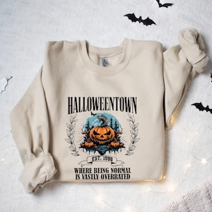 Może przedstawiać: Beżowa bluza z nadrukiem graficznym przedstawiającym dynię i tekstem "HALLOWEENTOWN EST. 1998 WHERE BEING NORMAL IS VASTLY OVERRATED".