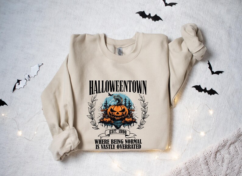 Może przedstawiać: Beżowa bluza z nadrukiem graficznym przedstawiającym dynię i tekstem "HALLOWEENTOWN EST. 1998 WHERE BEING NORMAL IS VASTLY OVERRATED".