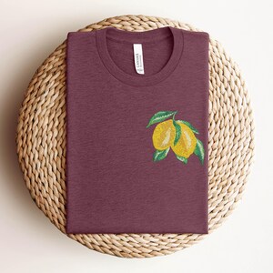 Puede incluir: Una camiseta color granate con un gr&aacute;fico de dos limones amarillos con hojas verdes.