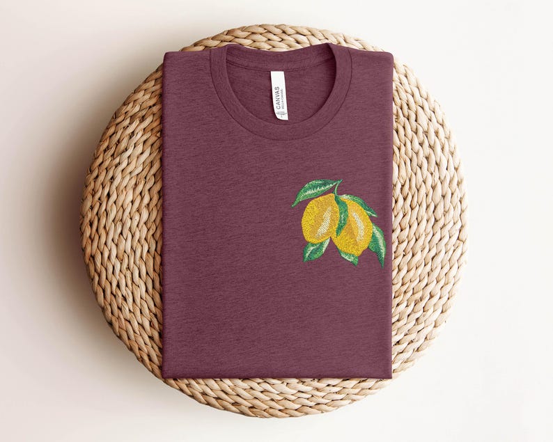 Puede incluir: Una camiseta color granate con un gr&aacute;fico de dos limones amarillos con hojas verdes.