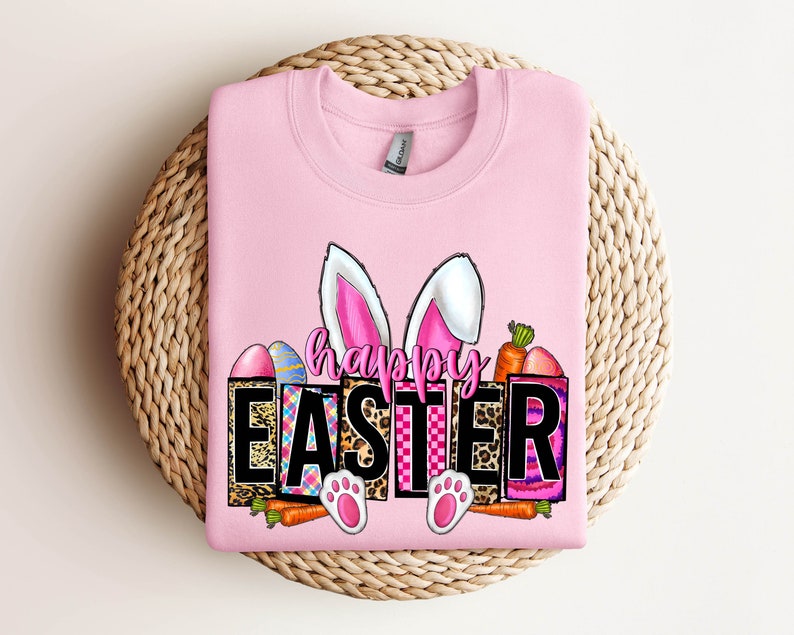 May include: Pink sweatshirt with a graphic design of bunny ears, carrots, and Easter eggs. The graphic says "Happy Easter" in black letters.