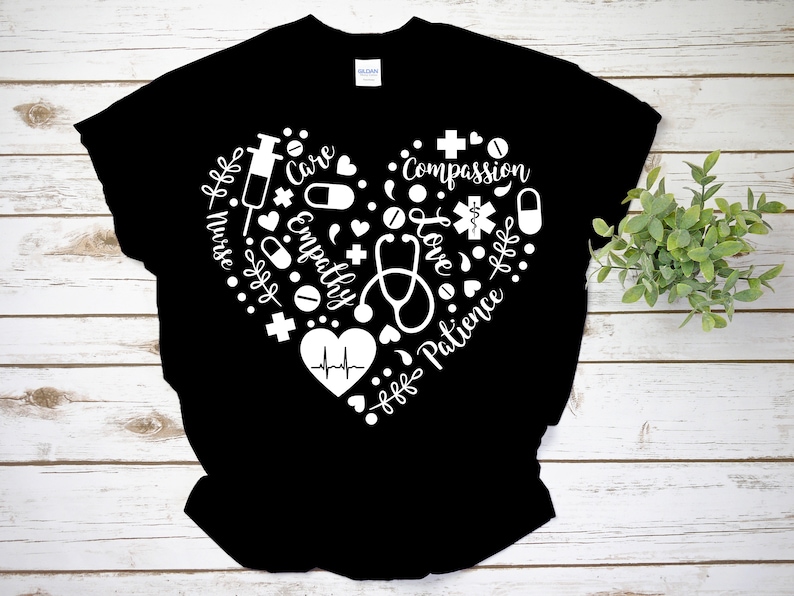 Puede incluir: Camiseta negra con un dise&ntilde;o de coraz&oacute;n blanco que presenta s&iacute;mbolos m&eacute;dicos y las palabras "Enfermera", "Cuidado", "Empat&iacute;a", "Compasi&oacute;n", "Amor" y "Paciencia".
