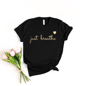 May include: Black t-shirt with the text "just breathe" in gold lettering and a small gold heart above the text.