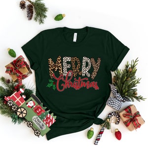 May include: A dark green t-shirt with the words "Merry Christmas" in red and white letters with a leopard print pattern. The letters are layered on top of each other and the word "Christmas" is slightly smaller than the word "Merry".