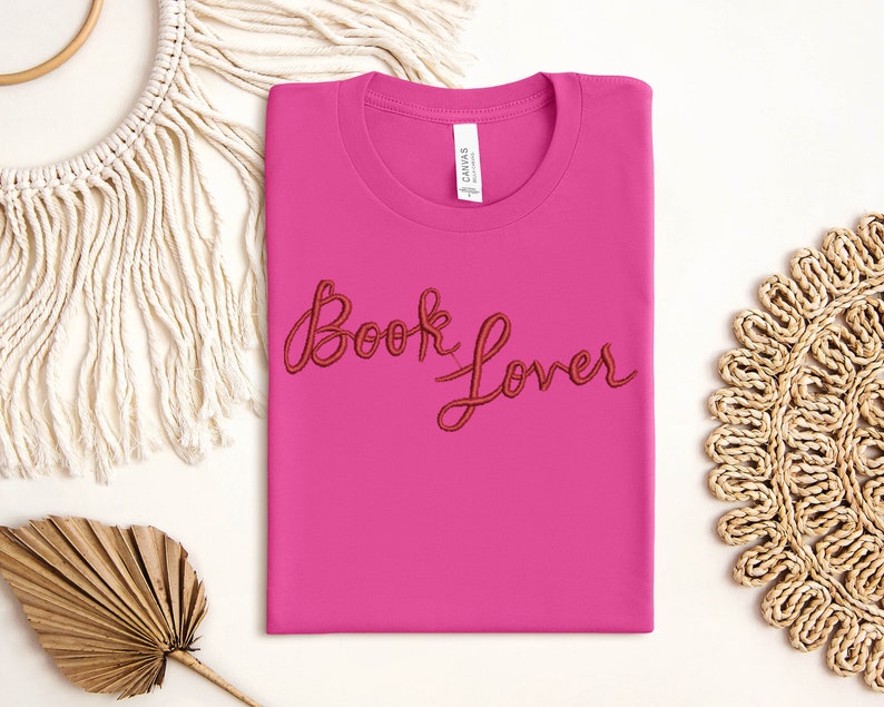 K&ouml;nnte beinhalten: Pinkes T-Shirt mit dem Schriftzug "Book Lover" in roter Stickerei.