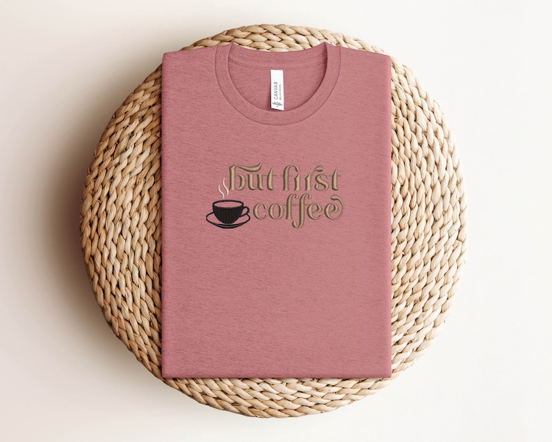 May include: A pink t-shirt with the text "But first coffee" in a gold font. A small black coffee cup with steam is above the word "coffee".