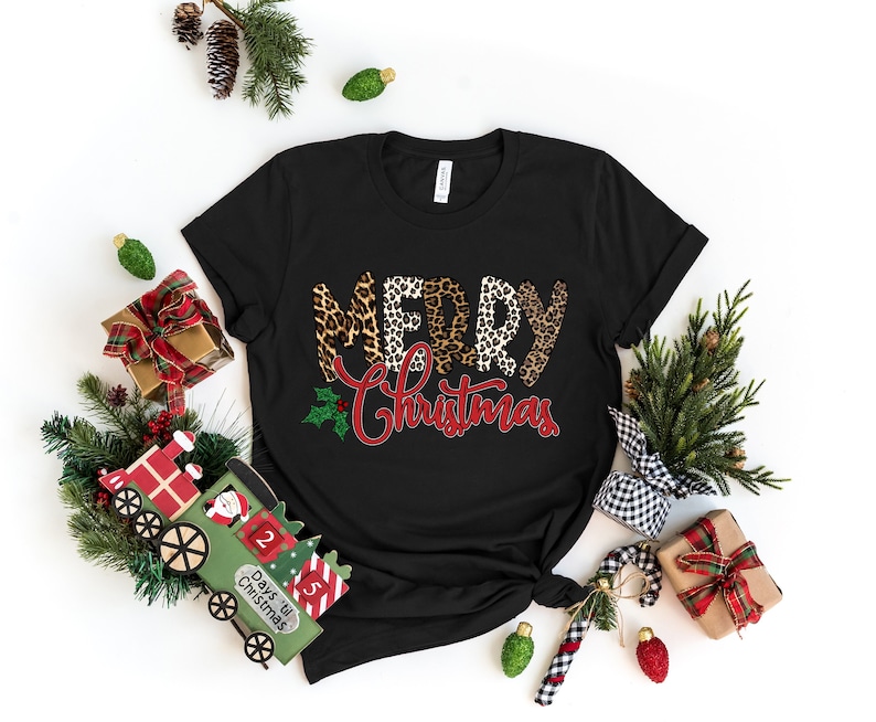 May include: Black t-shirt with a "Merry Christmas" design featuring leopard print letters and a red holly sprig.