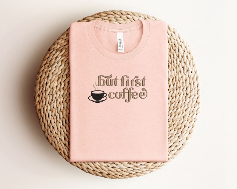 May include: A pink t-shirt with the text "but first coffee" and a small graphic of a coffee cup with steam coming from it.