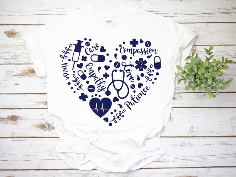 Puede incluir: Camiseta blanca con un dise&ntilde;o de coraz&oacute;n azul marino. El coraz&oacute;n est&aacute; lleno de s&iacute;mbolos m&eacute;dicos y las palabras "Enfermera", "Cuidado", "Empat&iacute;a", "Compasi&oacute;n", "Amor", "Paciencia".