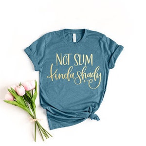 May include: A teal blue t-shirt with the text "Not Slim Kinda Shady" in gold lettering.