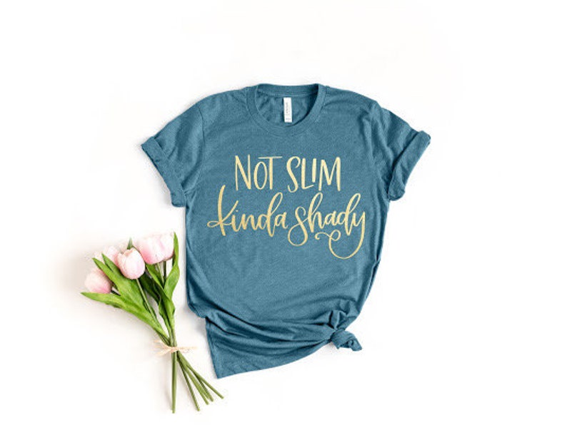 May include: A teal blue t-shirt with the text "Not Slim Kinda Shady" in gold lettering.