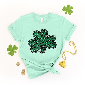 May include: A light green t-shirt with a green and black leopard print shamrock design.