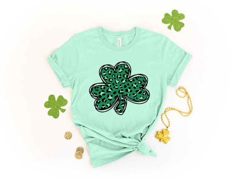May include: A light green t-shirt with a green and black leopard print shamrock design.