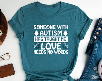 Op de afbeelding: Tealblauw T-shirt met witte tekst die luidt: "Iemand met *autisme* heeft me liefde geleerd die geen woorden nodig heeft".