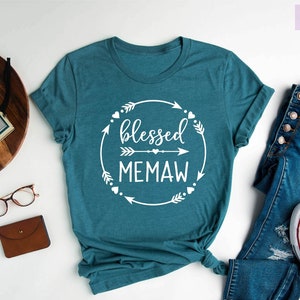 May include: Teal blue t-shirt with white text that reads "blessed memaw" in a circle with arrows and hearts.