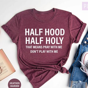 May include: A maroon t-shirt with the text "Half Hood Half Holy That means pray with me Don't play with me" in white lettering.