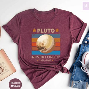 May include: A maroon t-shirt with a retro-style graphic of Pluto, the text "Pluto", and the text "Never Forget 1930-2006".