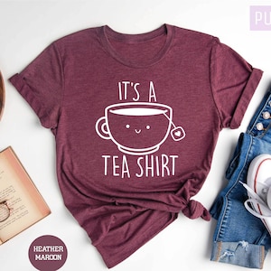May include: A maroon heather t-shirt with a white graphic of a teacup with a smiling face and the text "It's a Tea Shirt".