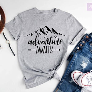 May include: Gray t-shirt with a black mountain range graphic and the text "adventure awaits" with an arrow on either side of the text.
