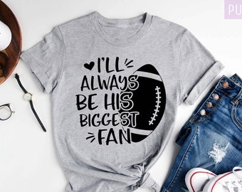 Könnte beinhalten: Ein graues T-Shirt mit dem Text "I'll Always Be His Biggest Fan" und einer schwarzen und weißen Fußballgrafik.