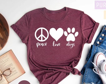 May include: A heather maroon t-shirt with a white peace sign, heart, and paw print graphic. The text "peace love dogs" is printed below the graphic.