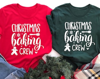 May include: Two t-shirts, one red and one forest green, with the text "CHRISTMAS BAKING CREW" in white. The design includes a snowflake, whisk, and gingerbread man. The shirts are displayed with denim jeans and holiday greenery.