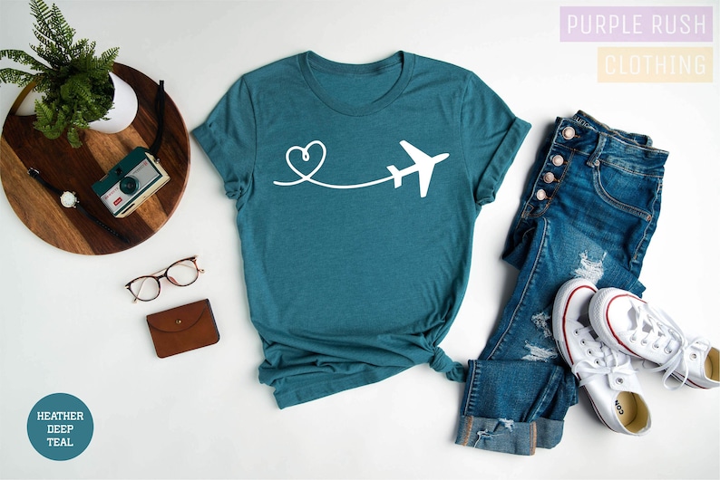 May include: A teal blue t-shirt featuring a white airplane and heart design. The text "Purple Rush Clothing" is in the top right corner of the image.