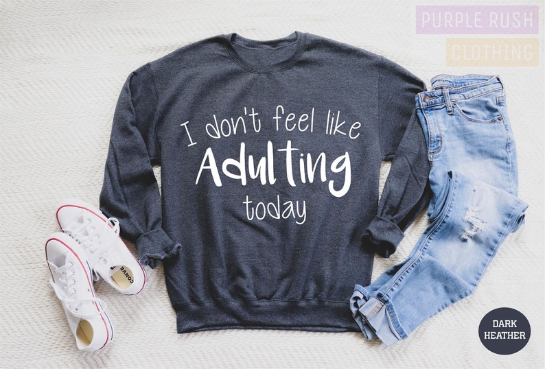 K&ouml;nnte beinhalten: Ein dunkel-helles graues Sweatshirt mit dem Text "I don't feel like Adulting today" in Wei&szlig;.