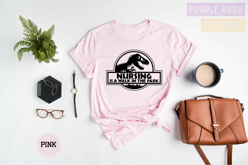 May include: Pink t-shirt with a black graphic of a dinosaur and the text "Nursing is a walk in the park".