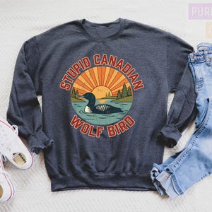 a gray sweatshirt with a graphic design, a pair of jeans, and a pair of white sneakers, all laid out on a white surface.