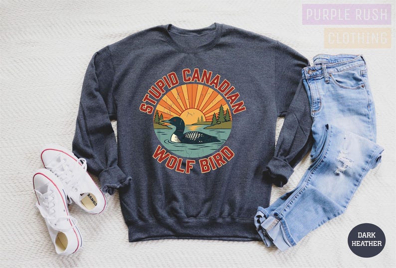 a gray sweatshirt with a graphic design, a pair of jeans, and a pair of white sneakers, all laid out on a white surface.