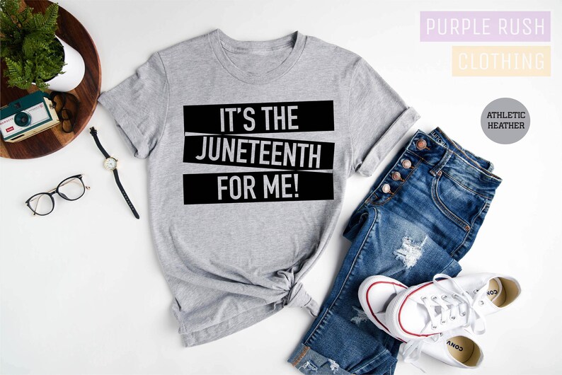 May include: A gray t-shirt with the text "It's the Juneteenth for me!" printed in black. The shirt is laid out on a white surface with a pair of jeans and white sneakers.