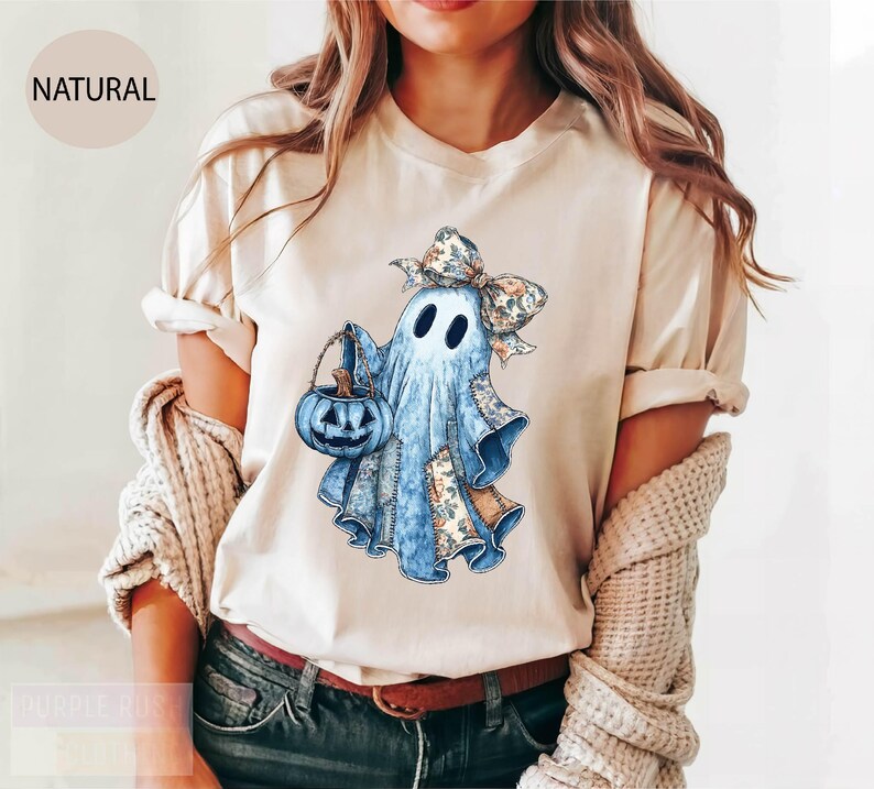 A woman wearing a white t-shirt with a graphic of a ghost holding a pumpkin and a bow.