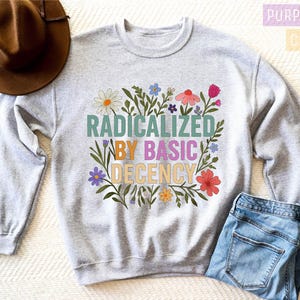 a gray sweatshirt with a colorful graphic design, a brown hat, and a pair of blue jeans, all laid out on a white surface.